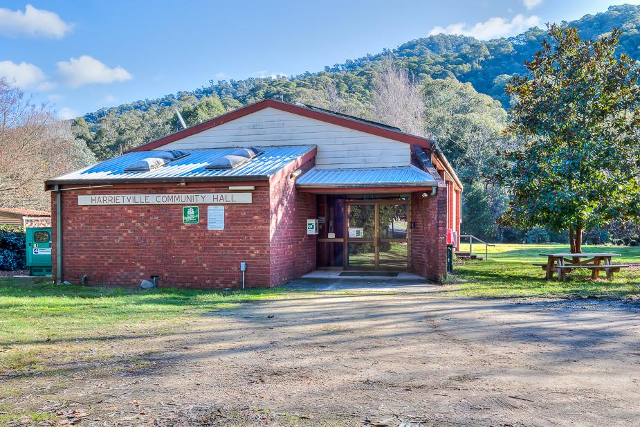 The exterior of Harrietville Hall, a brown brick single-story building with a recessed entryway to the right and a wooden sign stating Harrietville Community Hall on the brick wall to the left.