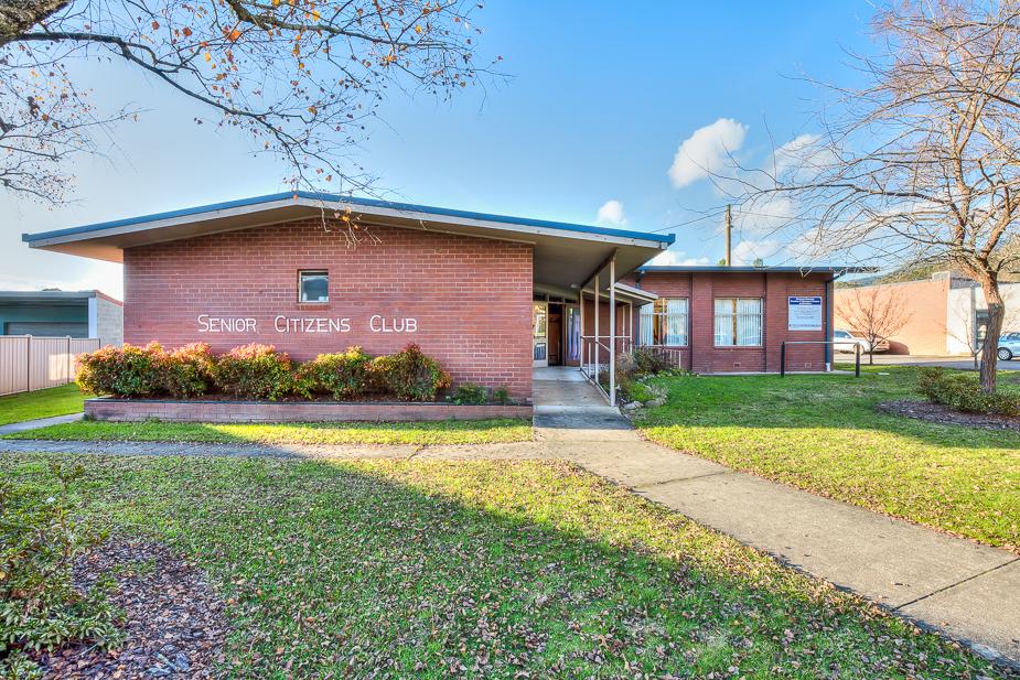 The exterior of the Mount Beauty Senior Citizens Centre, a red brick single-story building with a ramp leading up to the glass doors.
