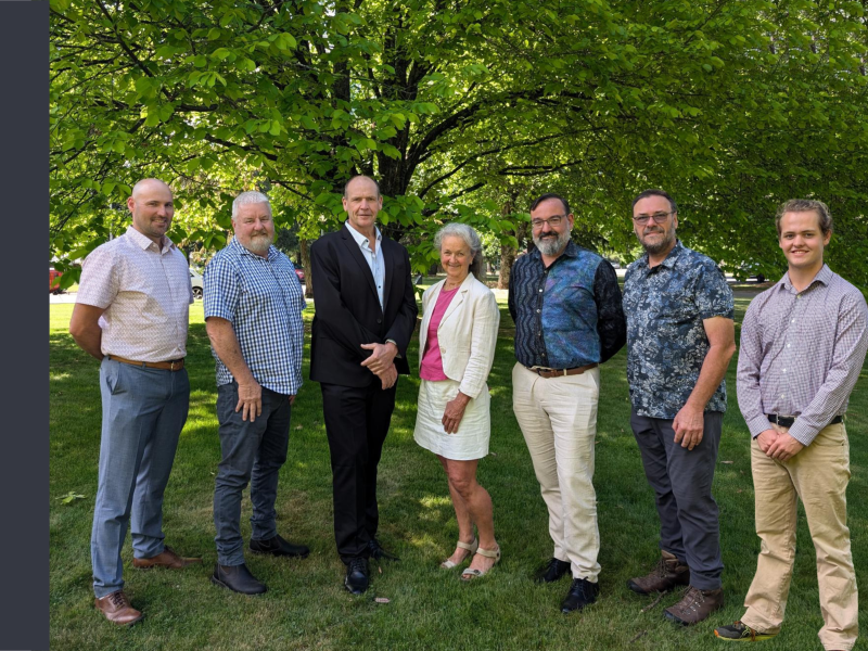 Seven Alpine Shire Councillors stand on grass with a tall tree behind them, obscuring the background. There are seven men and one woman.