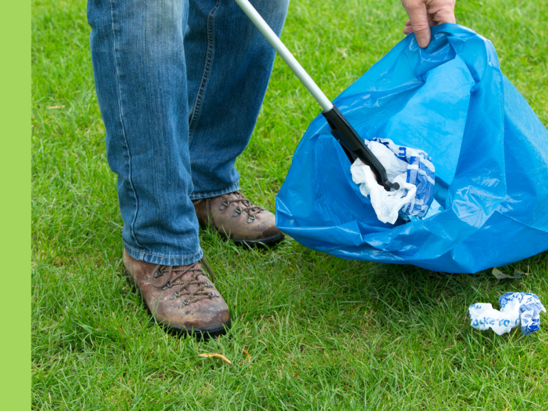 A person wearing dark blue jeans and brown hiking boots is picking up rubbish.
