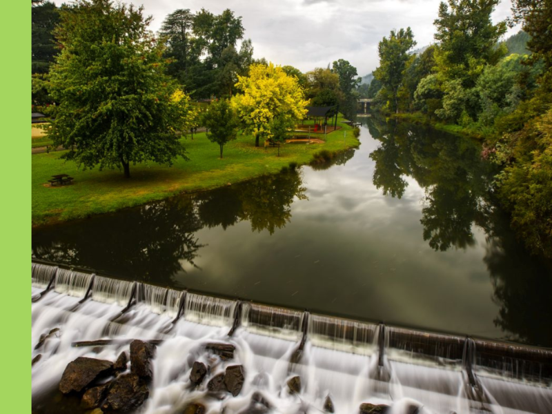 The Ovens River reflecting clouds above, with lush green lawn on the riverbank.