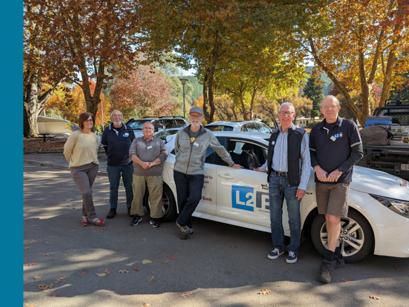 Six people standing in front of a white car that says L2P on the side.