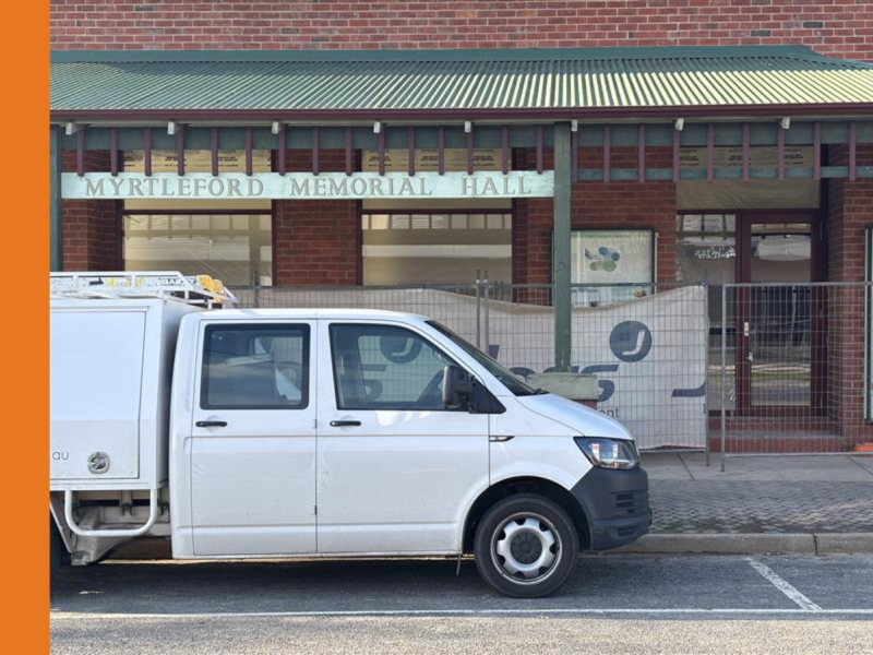 A white tradesperson's ute is parked outside of Myrtleford Memorial Hall, which has fencing erected in front of the building.