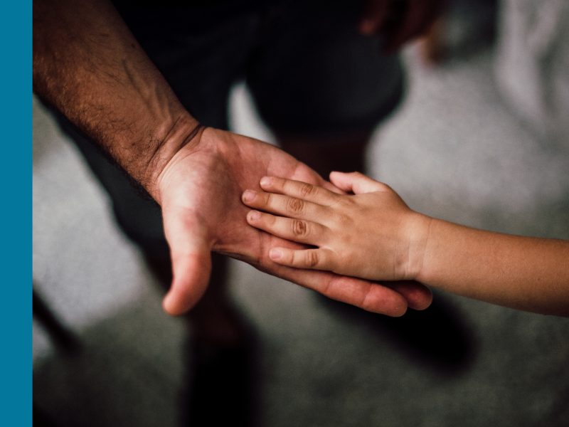 Two hands - one belonging to an adult and one to a child - palm to palm suggesting they are caring and supportive of one another.