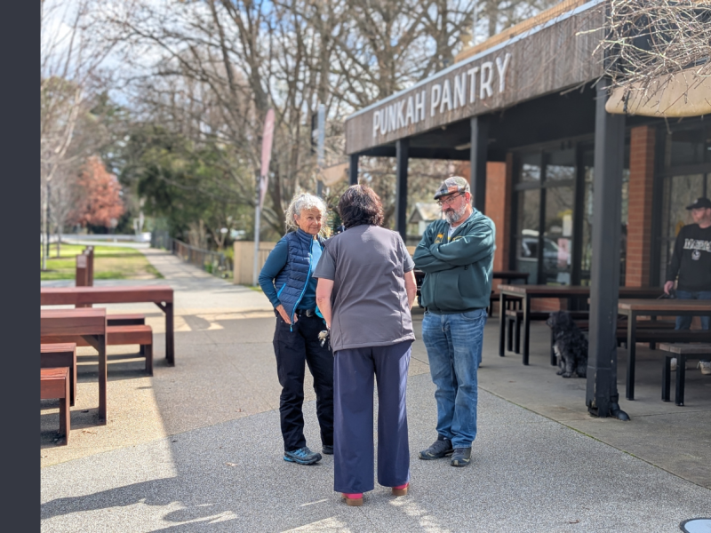 Three people stand in front of a cafe with a sign stating Punkah Pantry.