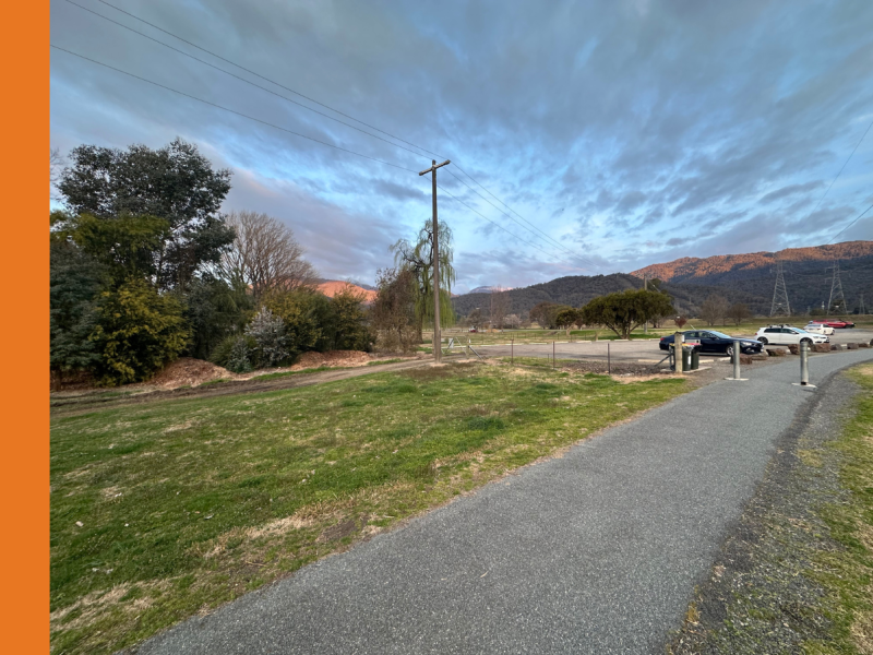 A concrete footpath next to a grass area leading to a carpark.