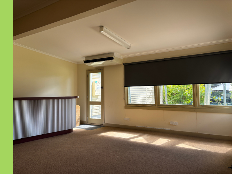 A room with a door in the left corner and windows with the blinds pulled halfway down.