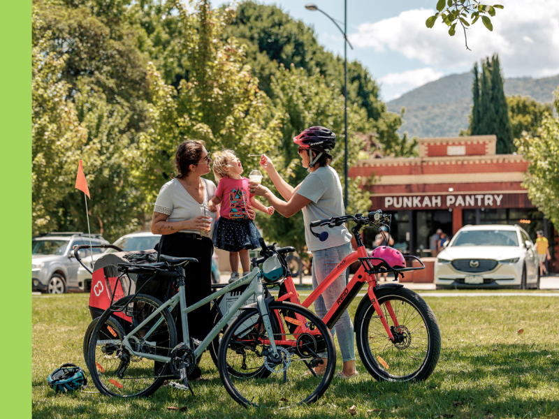 Two women feed their child ice cream across the road from a cafe that says 'Punkah Pantry'.