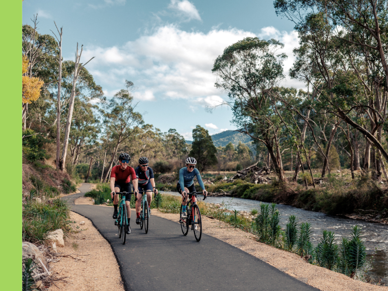 Three cyclists ride along an asphalt riding track next to a river.