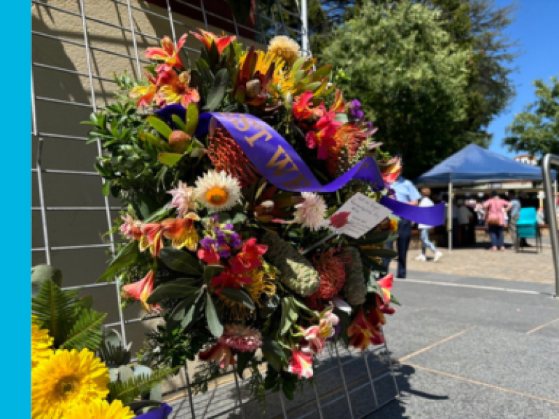 A wreath of flowers with a purple ribbon on it that says Lest We Forget.