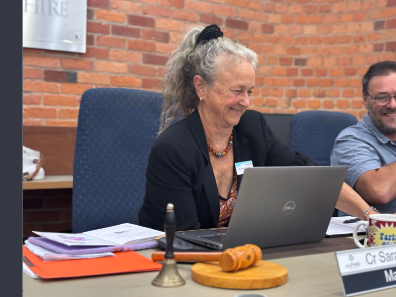 A woman with long grey hair in a high ponytail is smiling while looking down at an open laptop in front of her.