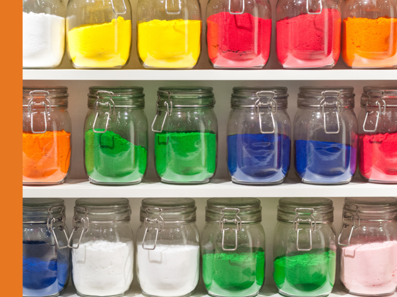 Mason jars neatly stacked on a shelf with brightly coloured sand inside them.