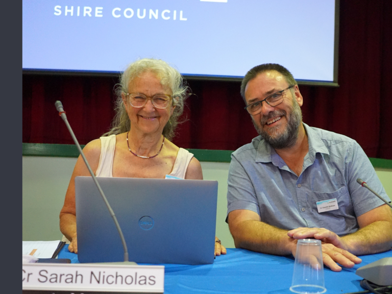 A woman with grey hair and a man wearing glasses and a blue shirt are smiling at the camera.