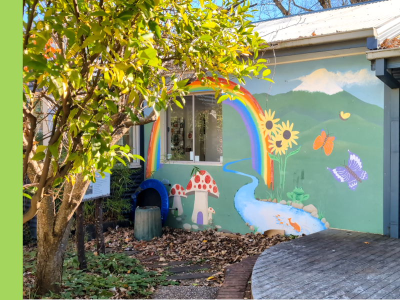 A wall with a colourful mural showing a snow-capped hill with a rainbow, sunflowers, butterflies, and mushrooms along a river.