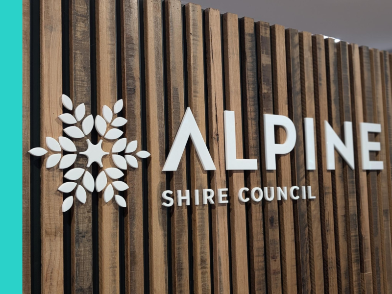 Timber slat wall with the white Alpine Shire logo attached to it, featuring a white snowflake and the words 'Alpine Shire Council' in white text.