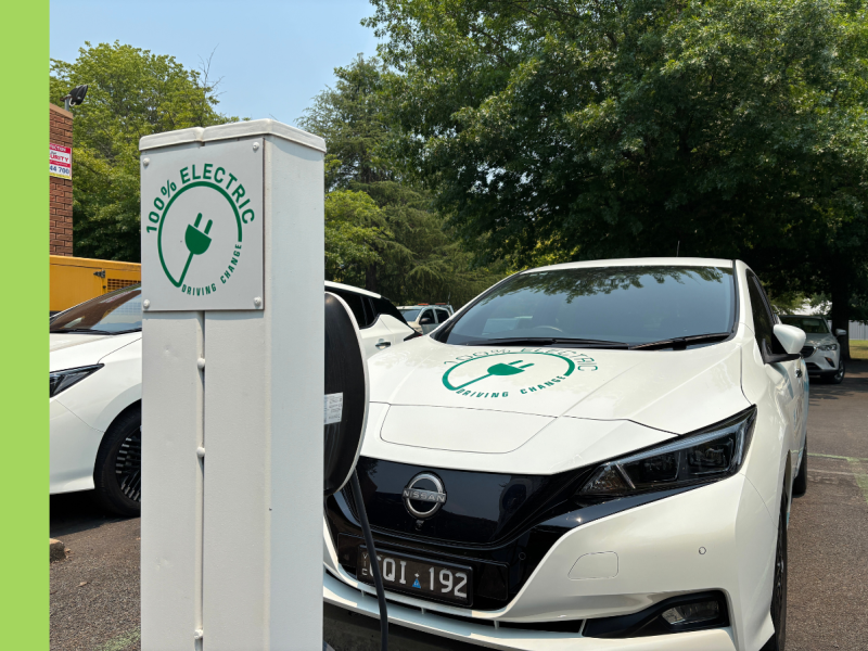 A white electric vehicle charger with a white electric vehicle parked in a parking bay.