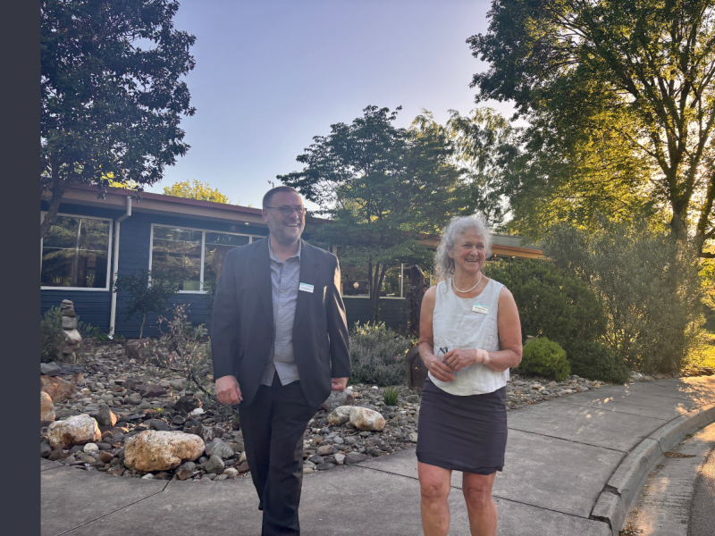 A man in a suit walks next to a woman wearing a sleeveless white shirt and a dark skirt.