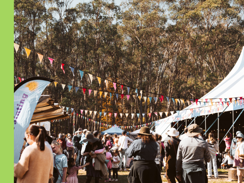 An event in a bush setting with lots of people walking around, featuring coloured bunting strung across the image, and a large marquee in the background.