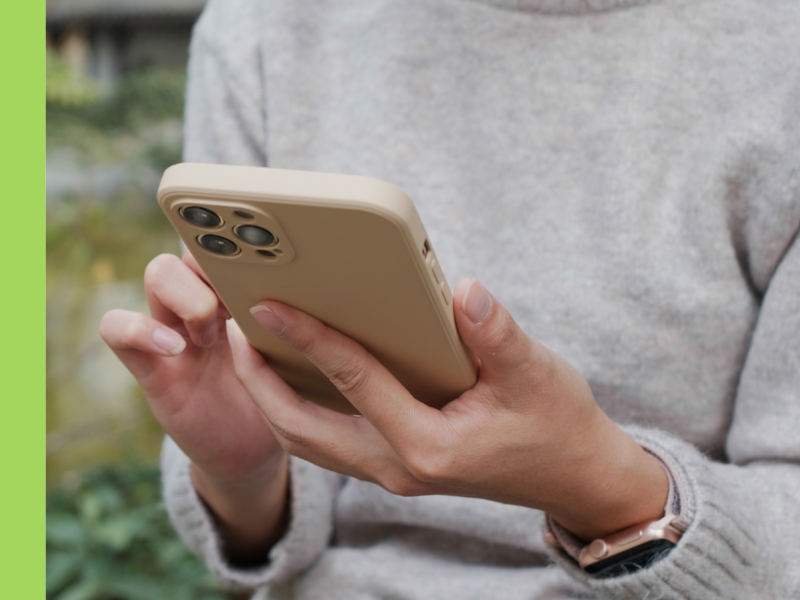 A woman's hands holding and using a smartphone in a cream colour case. She is wearing a grey knitted jumper. Only her torso, arms and hands are in the photo.
