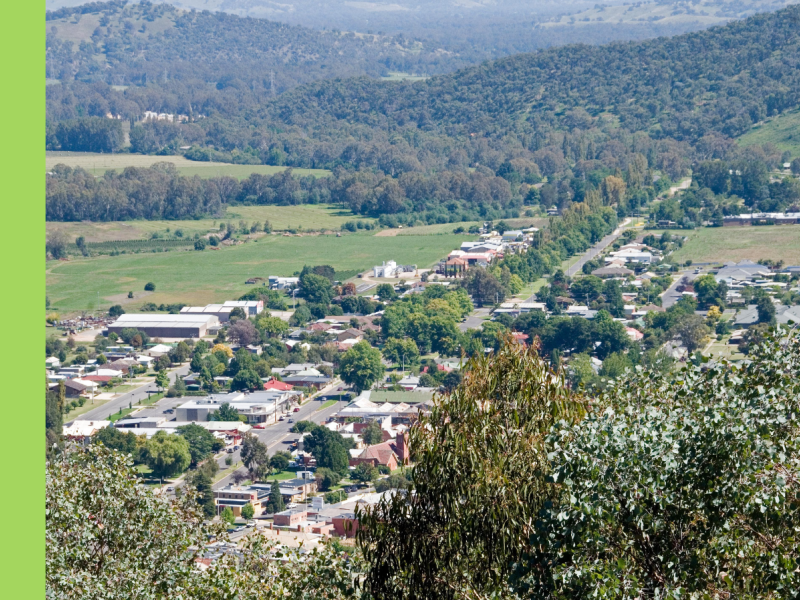 An aerial photo of a rural town with a main street, lined with trees, leading towards hills.