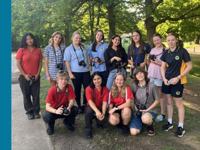 A group of eleven young people and one adult holding cameras and smiling at the camera.