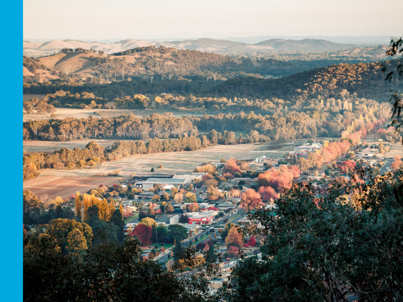 An aerial photo of a main street in a rural town with autumn trees lining the street and hills in the background.