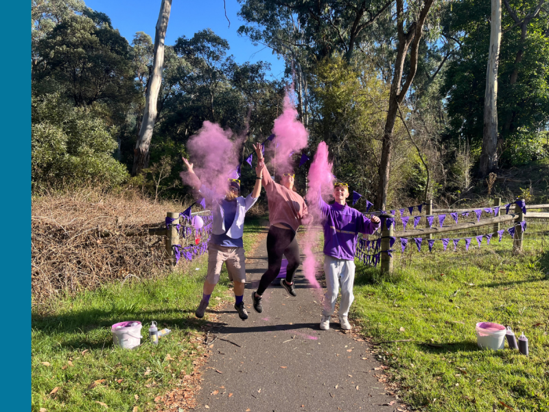 Three people throw purple coloured powder in the area as part of a Colour Fun Run.