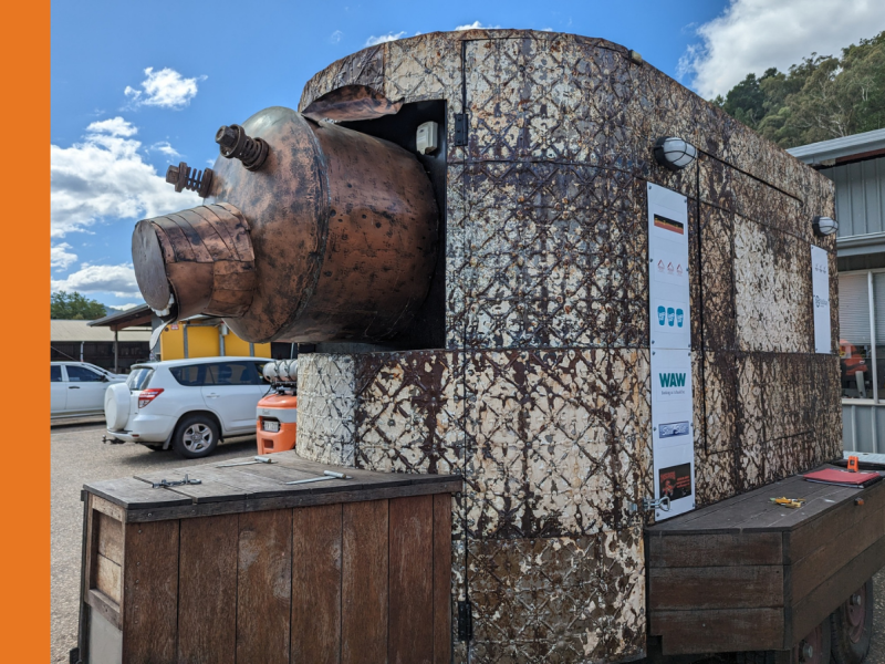 A metal van with a metal pig head sticking out one end of it.
