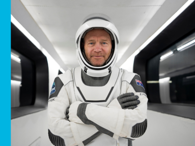 Eric Philips stands in a space craft with his crossed looking directly at the camera wearing a space suit, including helmet.