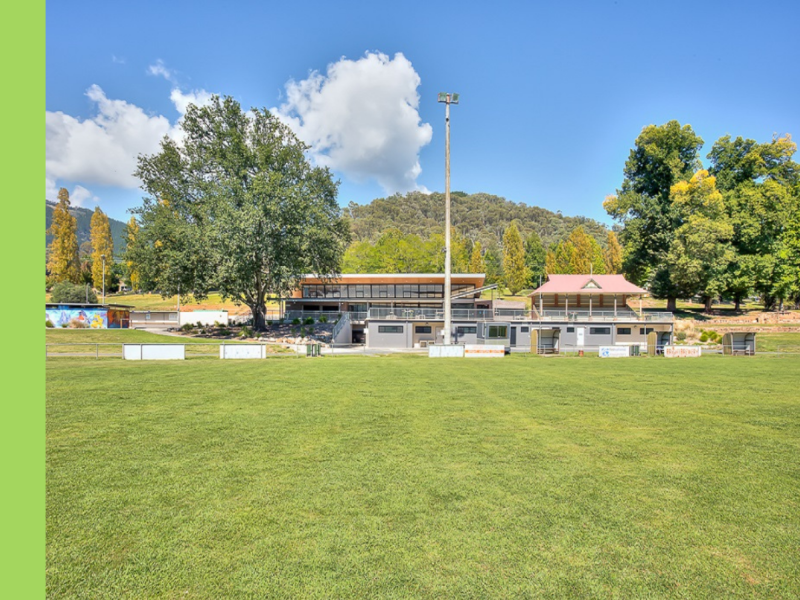 A sporting oval with a double storey building at the end of it.