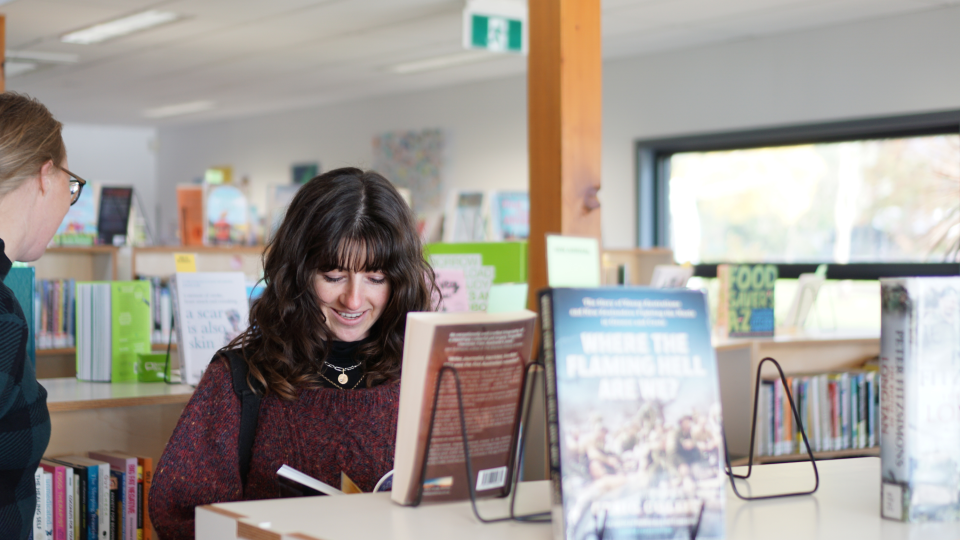 The interior of Mount Beauty with a young woman looking at a book, partially obscured by a book stack.