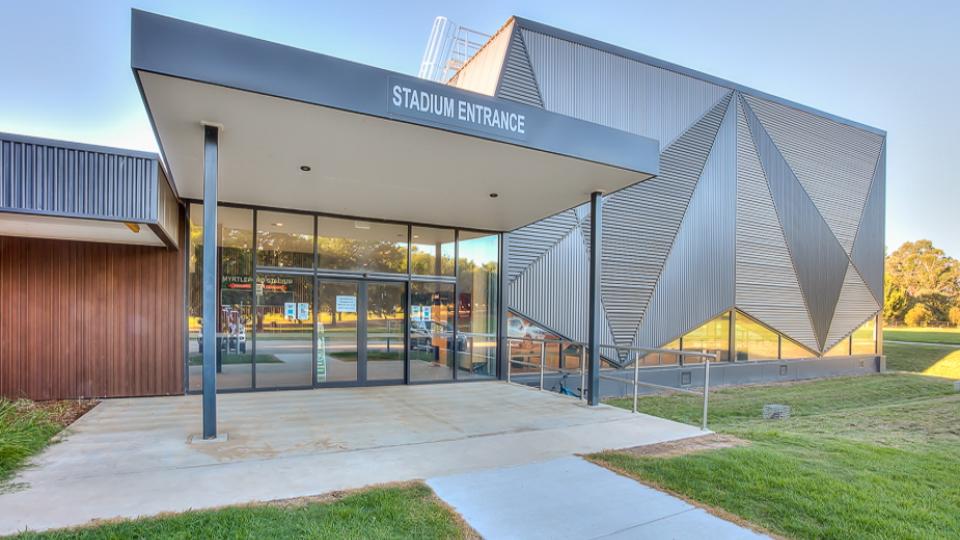 The Myrtleford Indoor Sports Stadium has a square verandah over the entryway, which has glass doors into the building. The left of the building has been designed using triangles, making it look futuristic.
