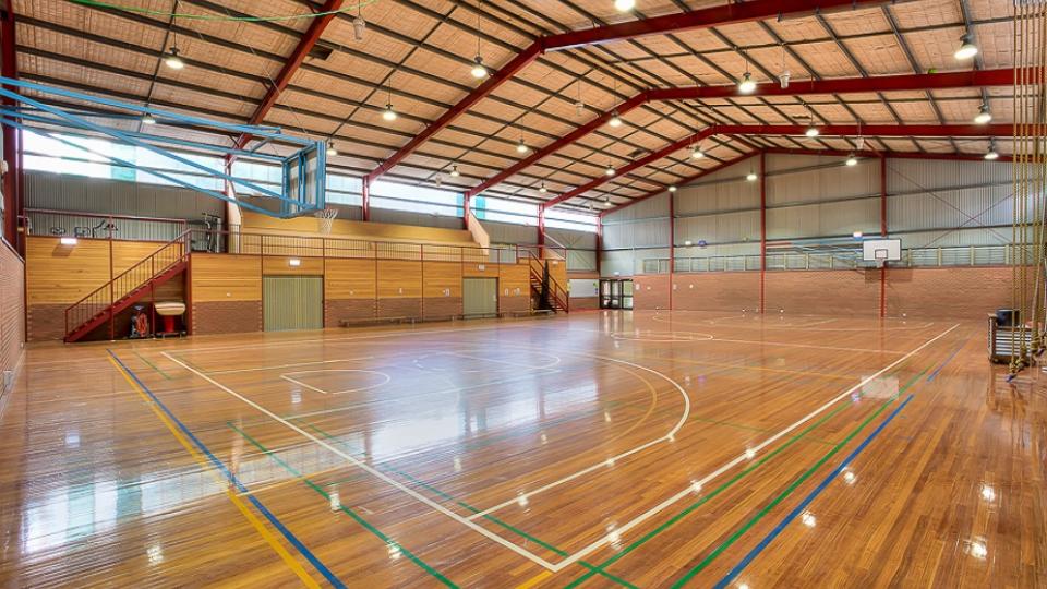 Mount Beauty Stadium is a multi-use stadium with multiple courts painted onto its floor, including basketball and volleyball. There are stairs with tiered seating to one side.