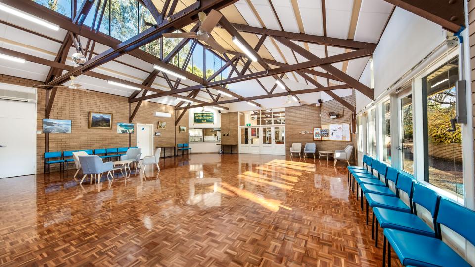 Fish-eye image of interior of Bright Senior Citizens Centre. There are blue chairs lined up on either side of the room.