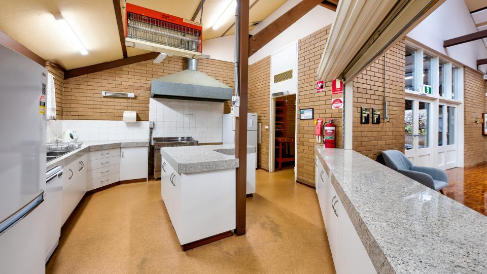 Interior image of the kitchen in Bright Senior Citizens Centre, with white cabinetry and marble-looking countertops. There is a roller door above the main service area.