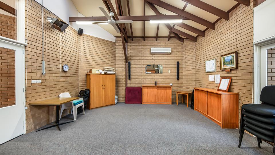 A room in Bright Senior Citizens Centre, with grey carpet and brick walls. There are various wooden cabinets and buffets against the walls of the room, with chairs stacked neatly beside them.