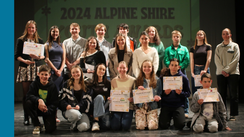 A group of individuals stands proudly on a stage, each holding a certificate of recognition. Behind them, a prominent banner displays the words '2024 Alpine Shire Youth Awards,' indicating a celebratory event honoring youth achievements. The setting suggests a formal awards ceremony, with participants dressed neatly and gathered for a commemorative photo.