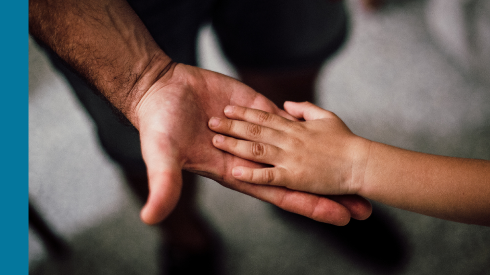 Two hands - one belonging to an adult and one to a child - palm to palm suggesting they are caring and supportive of one another.