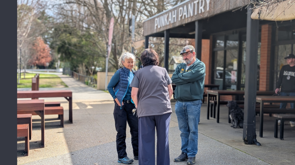 Three people stand in front of a cafe with a sign stating Punkah Pantry.