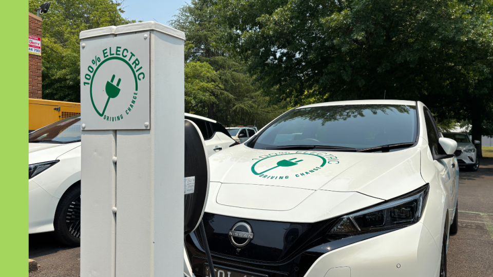 A white electric vehicle charger with a white electric vehicle parked in a parking bay.
