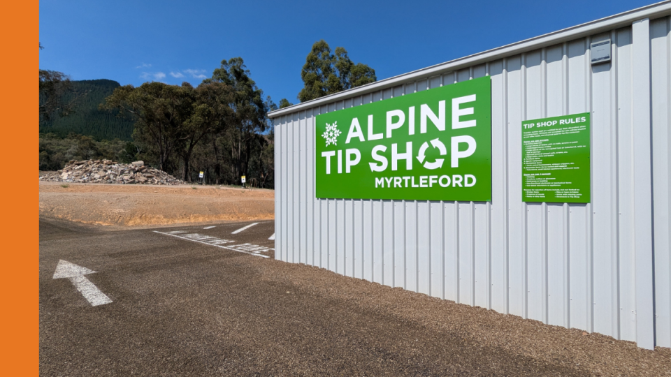The exterior of a corrugated iron shed with a green sign on the side that states Alpine Tip Shop Myrtleford.