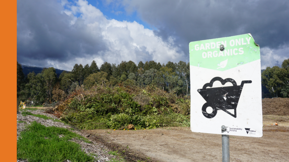 A sign states Garden Organics Only with a graphic of a wheelbarrow underneath. The sign is in front of a pile of green waste at a transfer station.